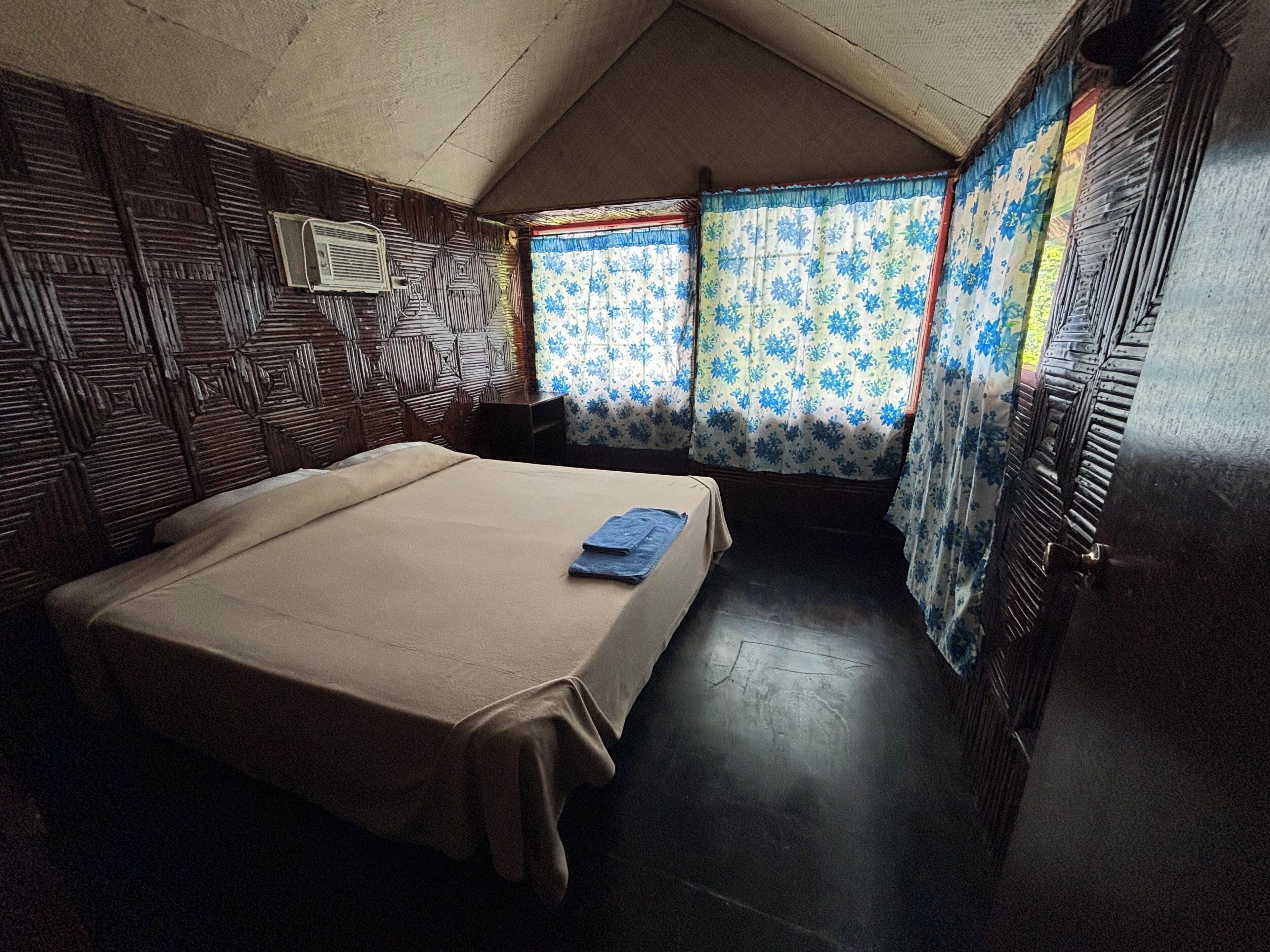 A room with a bed, a window with curtains, and a wooden headboard.