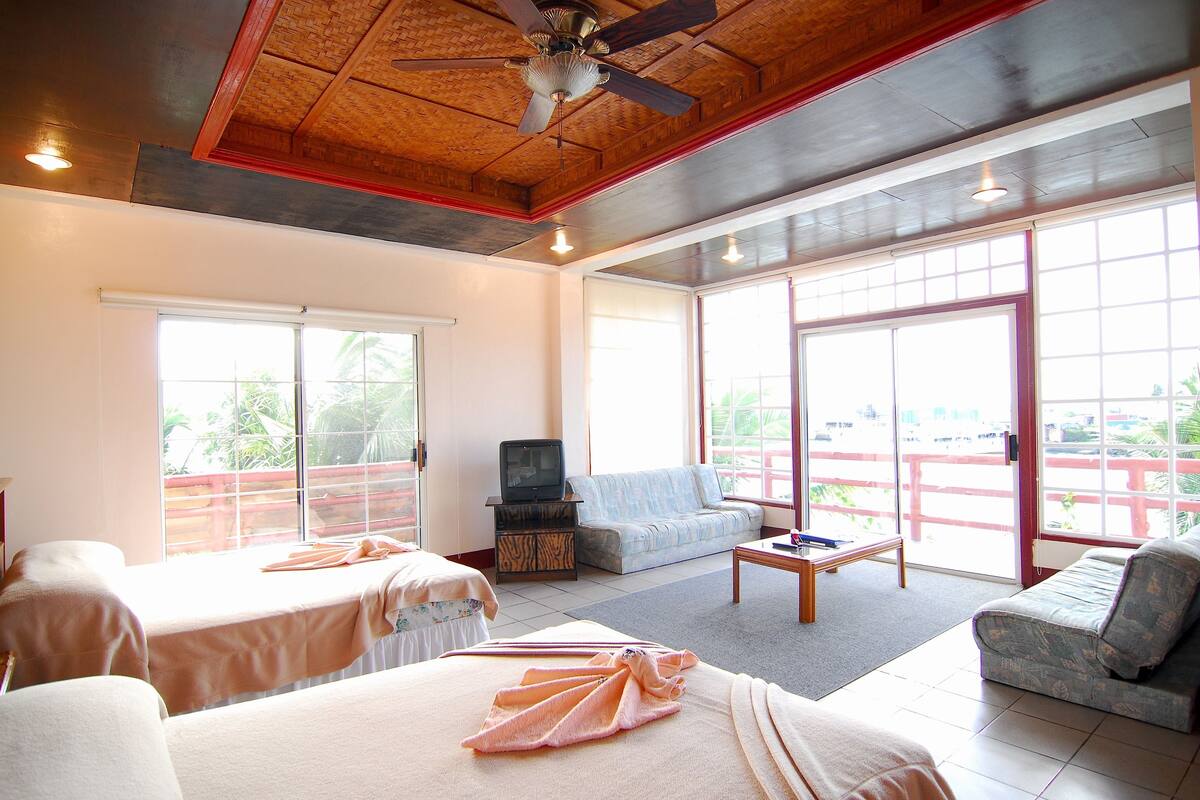 Habitación de hotel con dos camas, un sofá, un televisor y ventanas amplias.
