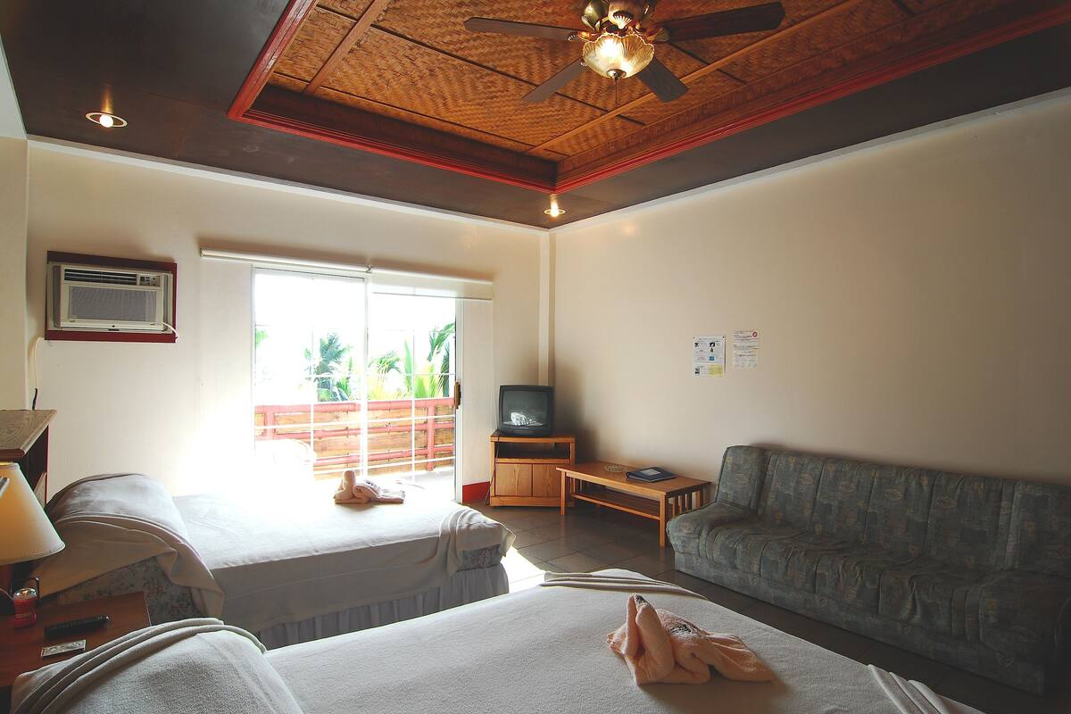 Habitación de hotel con dos camas, un sofá, un televisor y un ventilador de techo.