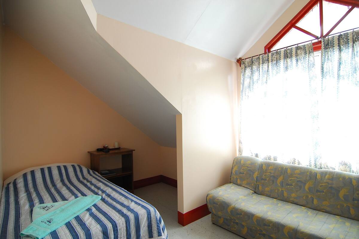 Una habitación con cama, sofá, una mesita y ventana con cortinas.