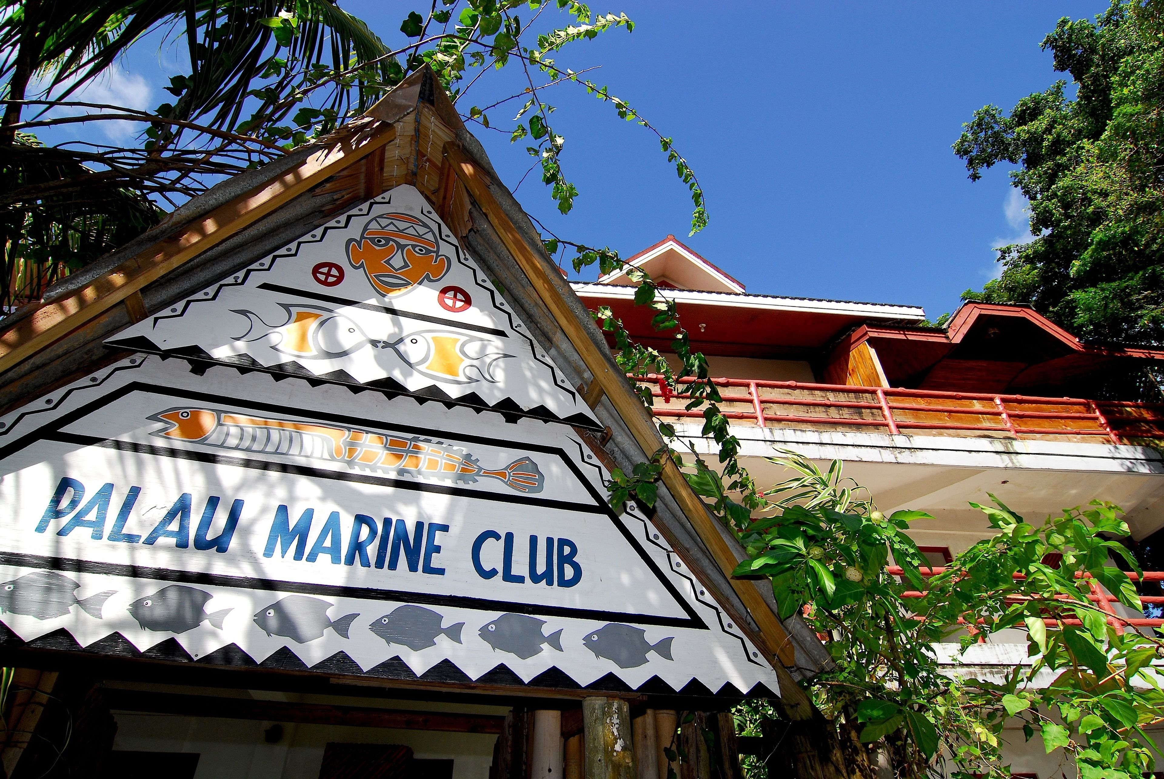 Rakennuksessa on kyltti, jossa lukee ”PALAU MARINE CLUB”, ja siinä on koristeellinen kalakuviokoriste.