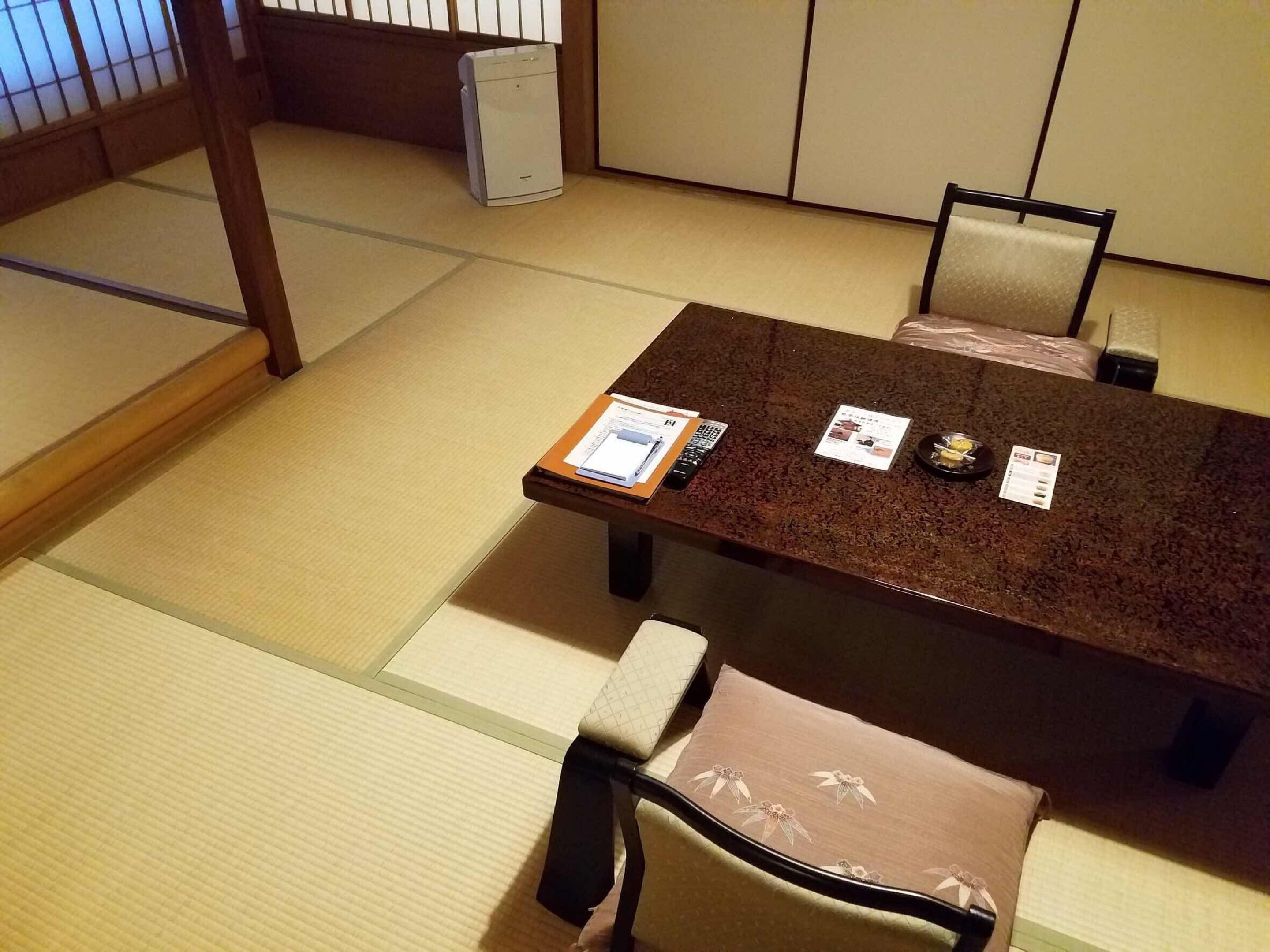 A traditional Japanese tatami room with a low table and chairs, a small heater, and a wooden screen in the background.