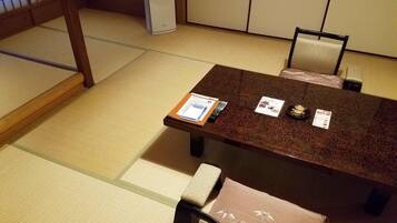A traditional Japanese tatami room with a low table and chairs, a small heater, and a wooden screen in the background.