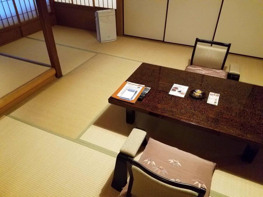 A traditional Japanese tatami room with a low table and chairs, a small heater, and a wooden screen in the background.