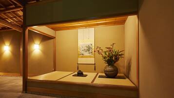 A traditional Japanese room with tatami flooring, a shoji screen, and a vase with flowers.