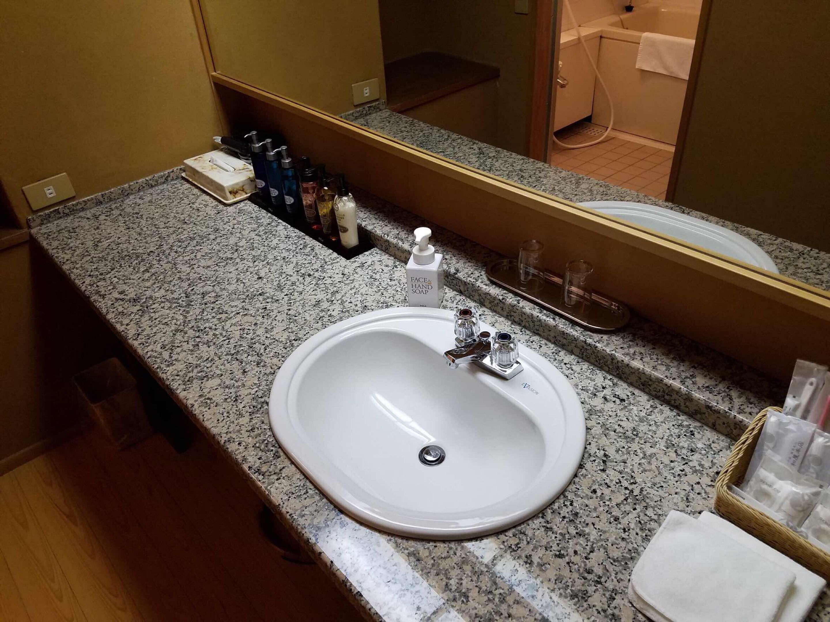 A hotel bathroom with a granite countertop, a white sink, and a mirror above it.
