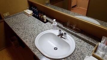 A hotel bathroom with a granite countertop, a white sink, and a mirror above it.