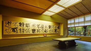 A room with a large calligraphy artwork on the wall, a tatami mat, and a view through a window.