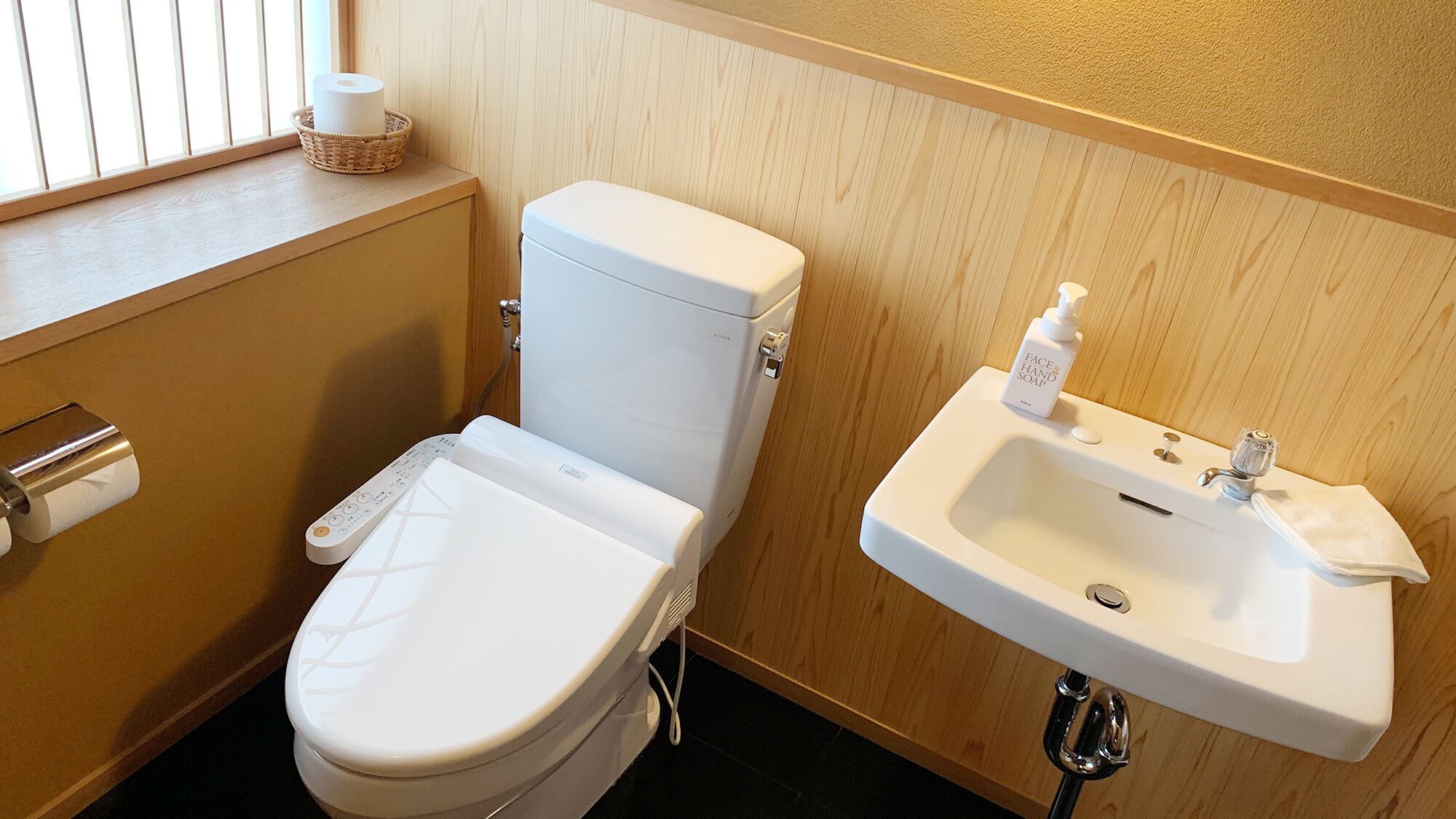 Een badkamer met toilet, een hygiëneschuimer, een wastafel en een raam met zonwering.