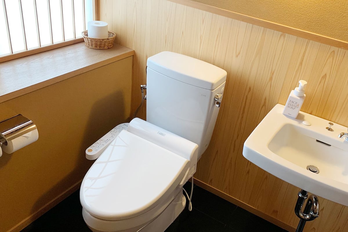 Une salle de bain comprenant des toilettes, un bidet, un lavabo et une fenêtre avec des stores.