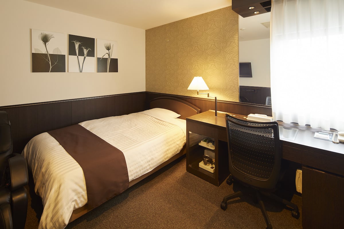 Une chambre d’hôtel avec un lit, un bureau, une chaise, une lampe et une œuvre d’art au mur.