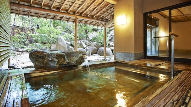 Een traditionele Japanse onsen met een houten terras, een rots als middelpunt en uitzicht op de omliggende tuin.