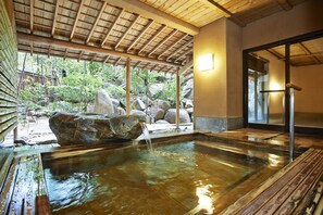 Un onsen japonés tradicional con una terraza de madera, una piedra central y vistas del jardín circundante.