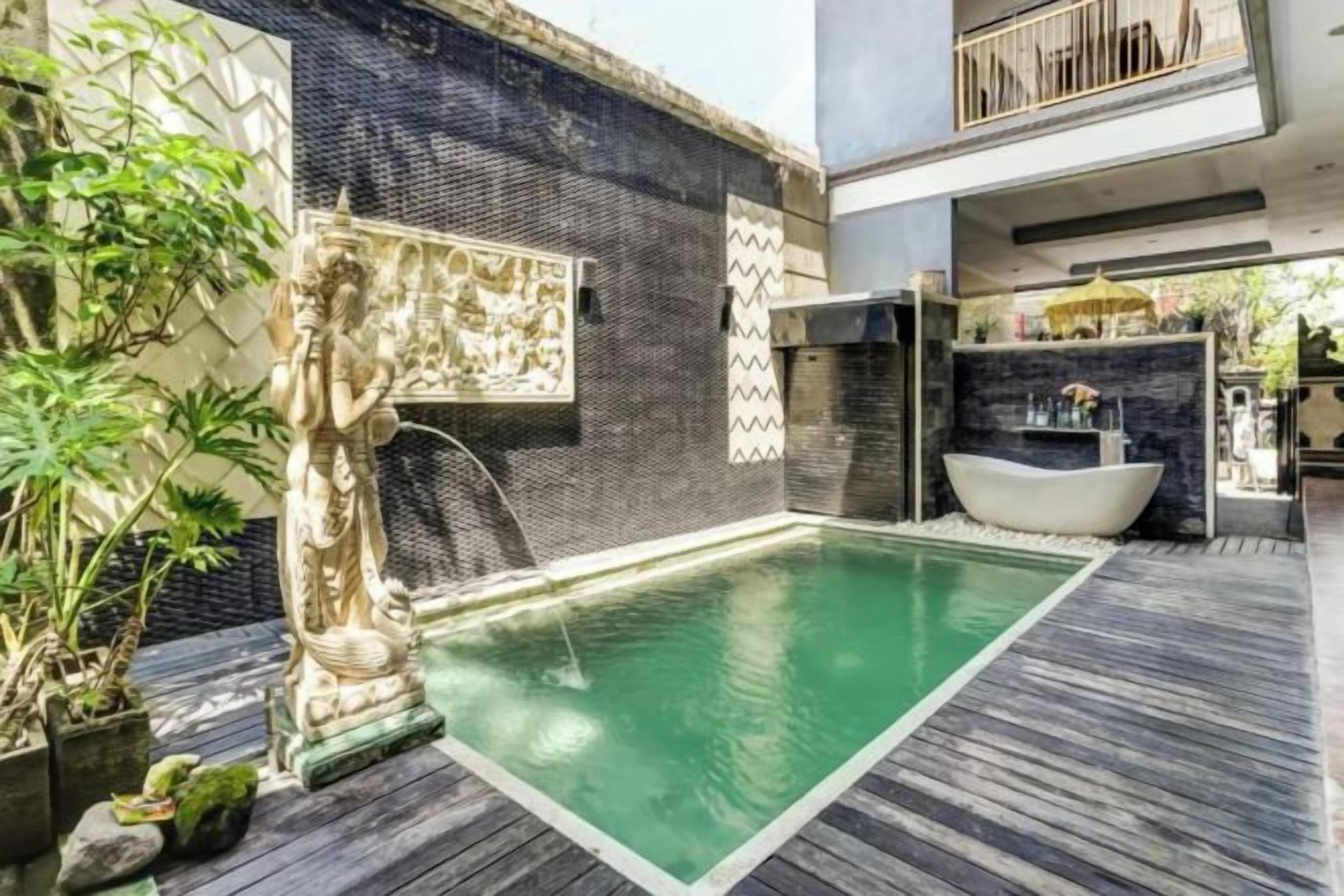 A swimming pool with a stone statue, a hot tub, and a wooden deck.
