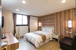 Una habitación de hotel con una cama, mesita de noche, lámpara y un escritorio con hervidor.
