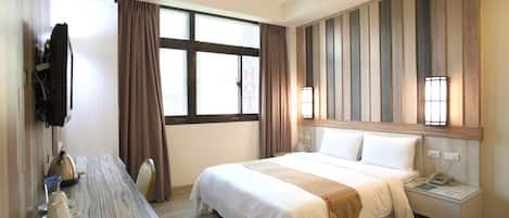 A hotel room with a bed, bedside table, and a desk with a kettle and tea set.