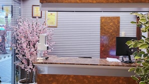 A reception desk with a modern design, featuring a metallic panel and a potted plant with pink flowers. - ChengDian Hotel (New Taipei City)