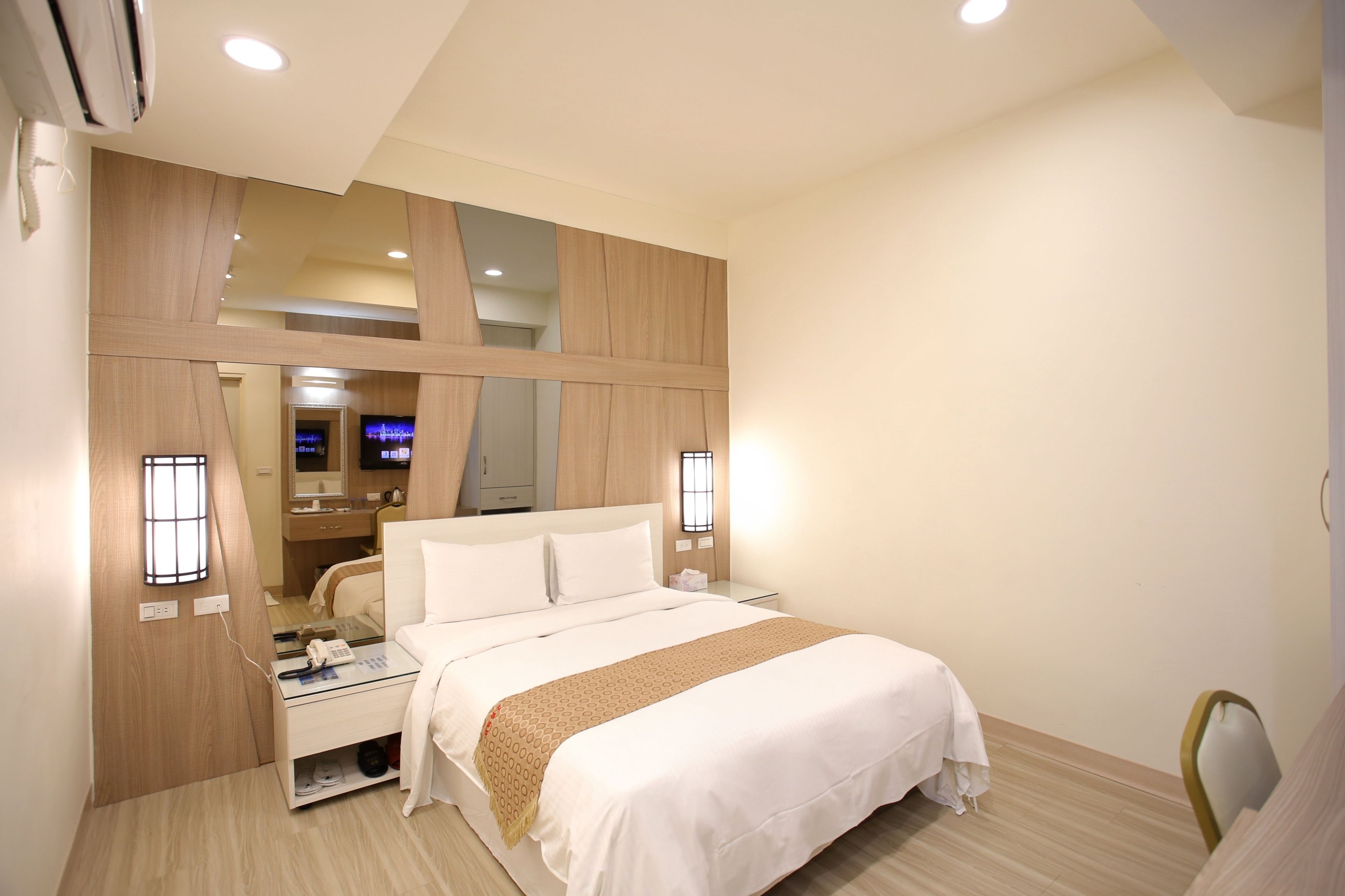 Una habitación de hotel moderna con una cama grande, mesitas de noche, un espejo y un televisor.