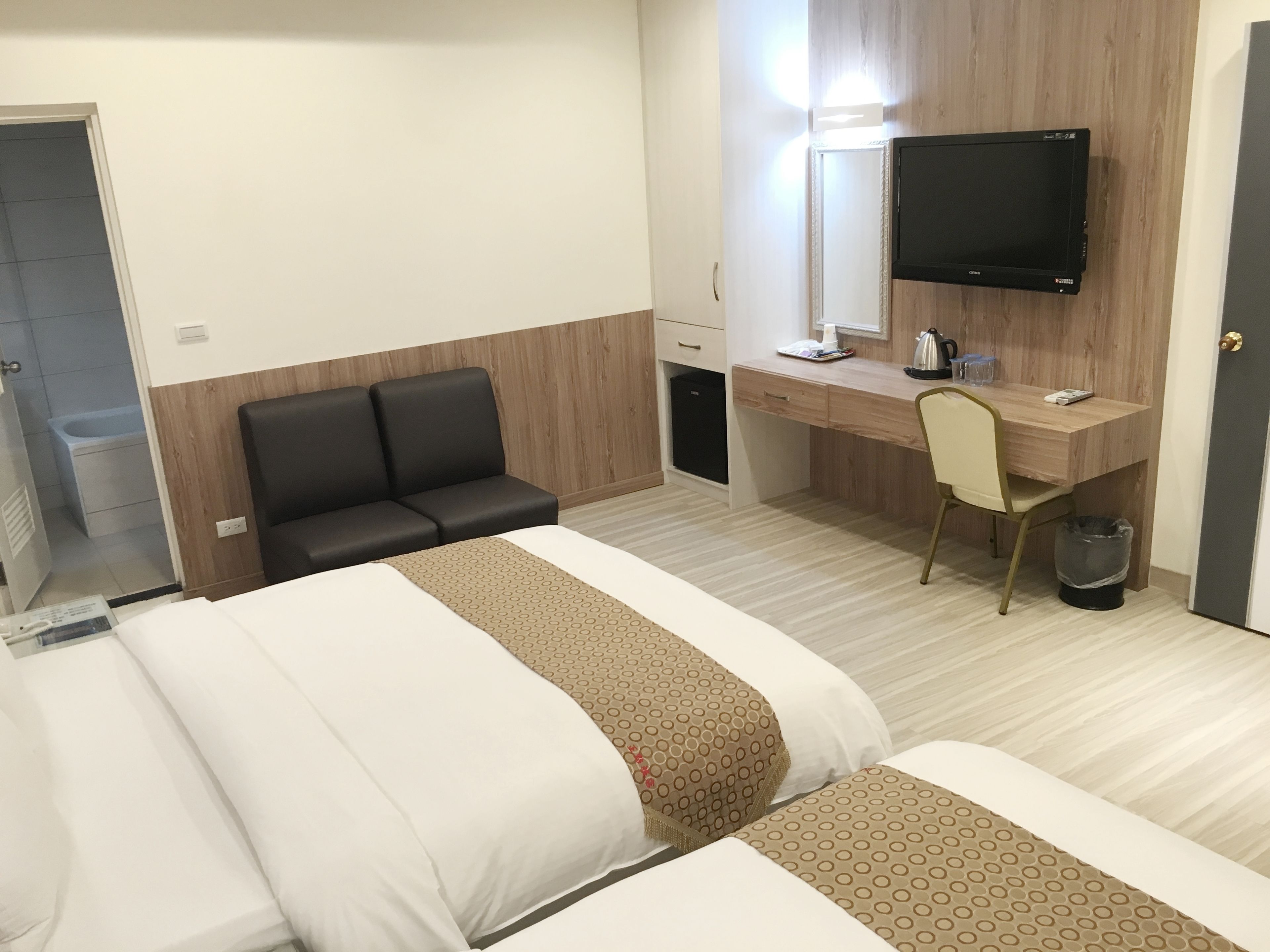 A hotel room with a bed, a desk, a chair, a television, and a small trash bin.