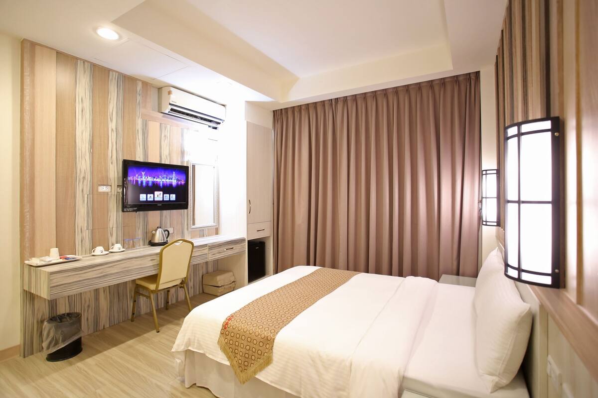 A hotel room with a bed, desk, chair, television, and curtains.