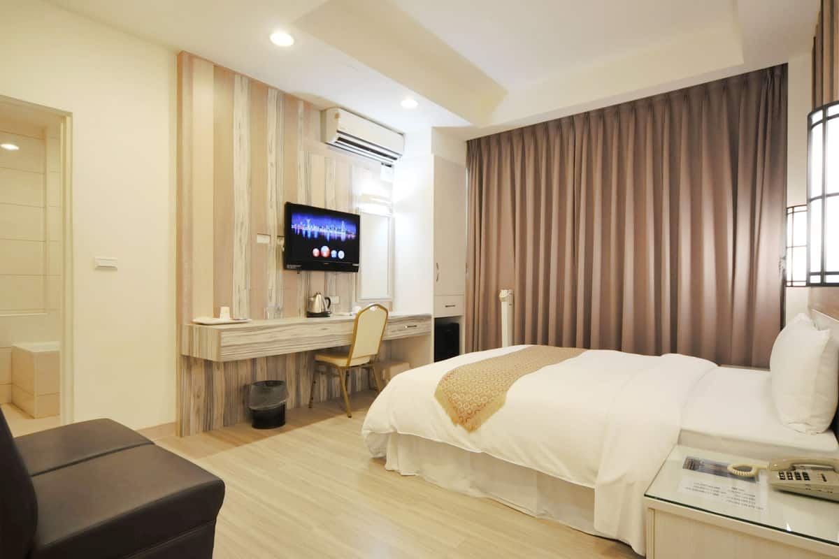 A hotel room with a bed, a desk, a chair, a TV, and a telephone.