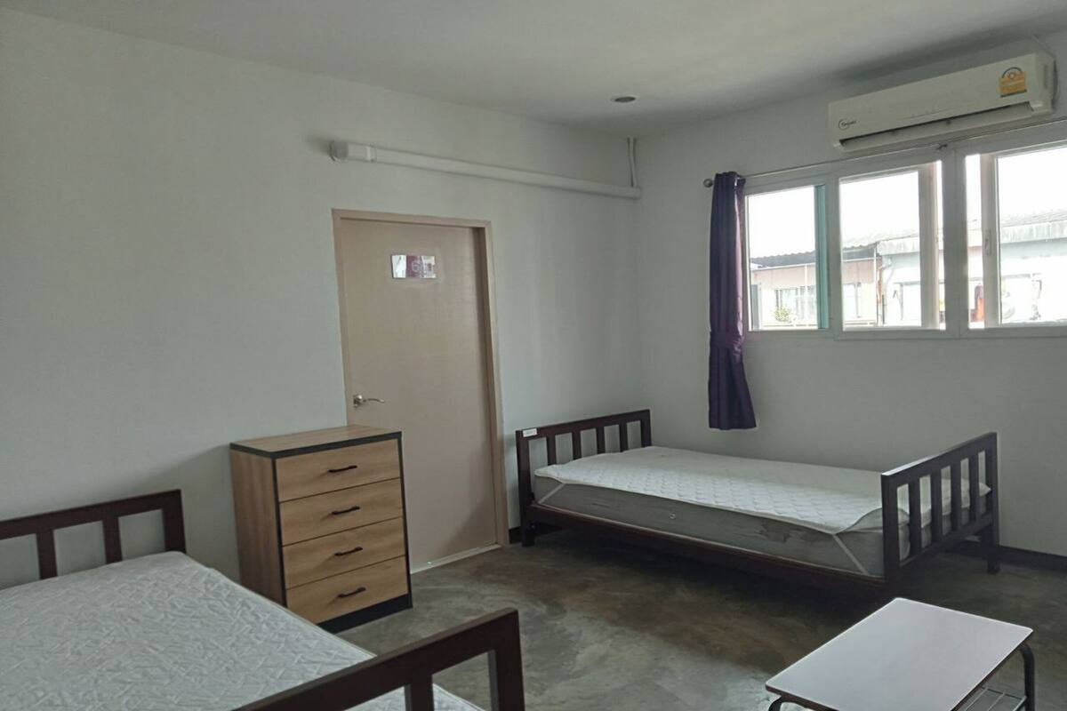 A room with two single beds, a wooden dresser, a small table, and a window with curtains.