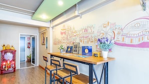A reception area with a wooden desk, chairs, a wall mural, and a small shrine. - Sleep Dee Hostel (Bangkok)