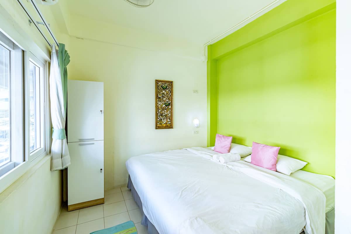 A bedroom with a bed, a wardrobe, a window with curtains, and a green accent wall.