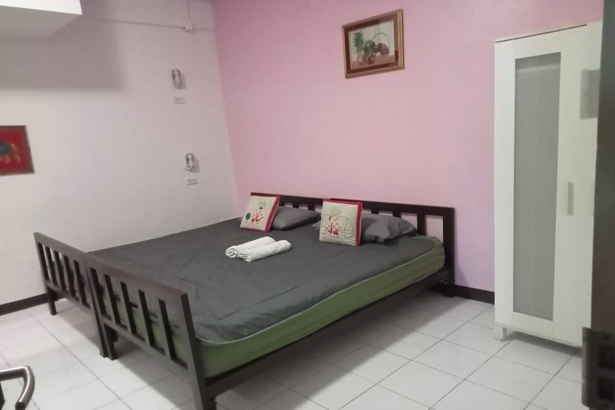 A single bed with a grey mattress and pillows, a wooden headboard, a white wardrobe, and a small framed picture on the wall.