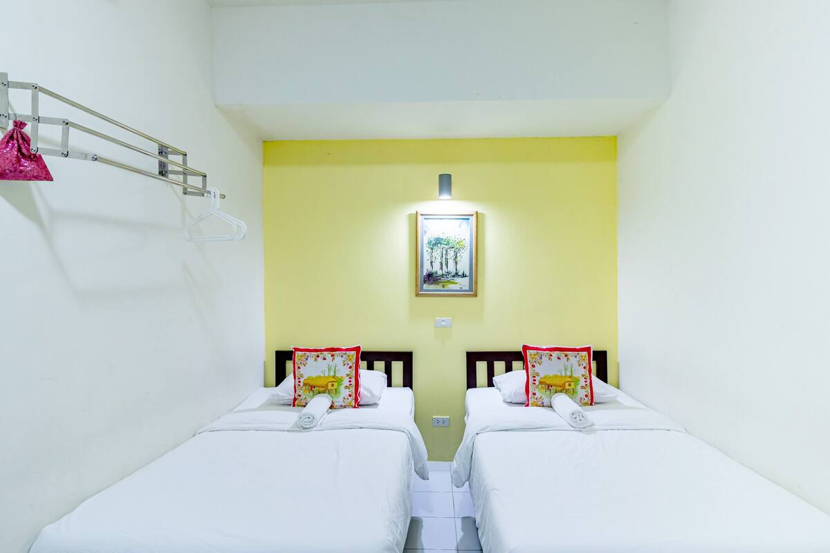 A room with two beds, a hanging bag rack, and a framed picture on the wall.