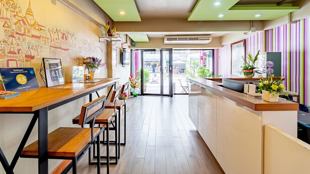A modern hotel lobby with a long reception desk, wooden benches, and a mural of a temple on the wall. - Sleep Dee Hostel (Bangkok)