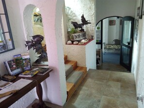 A hallway with a staircase leading to a room, a wooden table with books and a sculpture, and a wall with a bird sculpture and a framed picture. - Te Aputa Lodge (Te Puru)