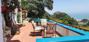 A terrace with outdoor seating, a pool, and a view of the sea. - Te Aputa Lodge (Te Puru)