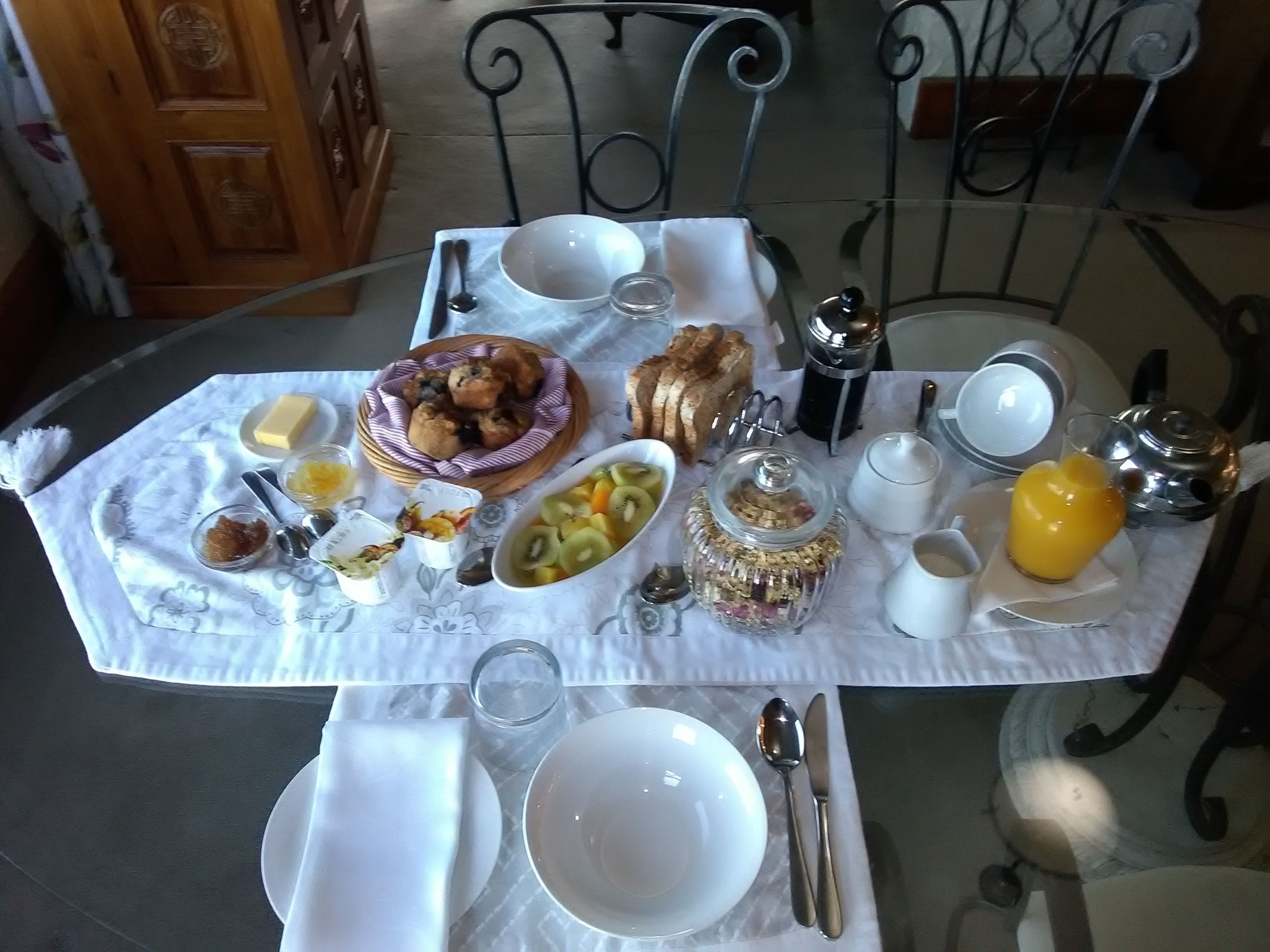 Una mesa de desayuno con diversos alimentos, como tostadas, muffins, fruta y un vaso de zumo de naranja.
