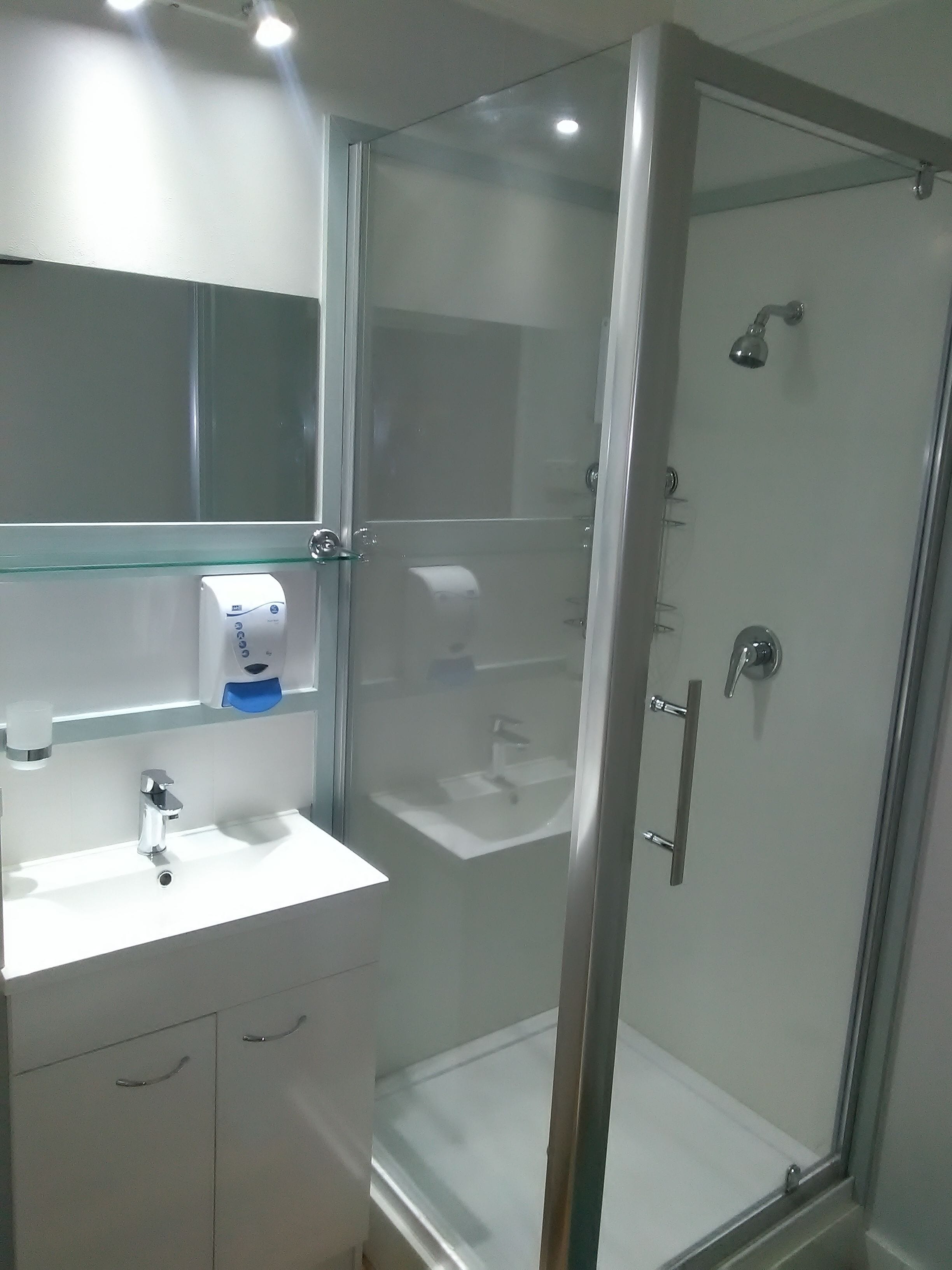 Un bagno moderno con cabina doccia in vetro, un lavandino bianco con specchio sopra e una mensola in vetro con dispenser di sapone.