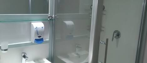 Un bagno moderno con cabina doccia in vetro, un lavandino bianco con specchio sopra e una mensola in vetro con dispenser di sapone.
