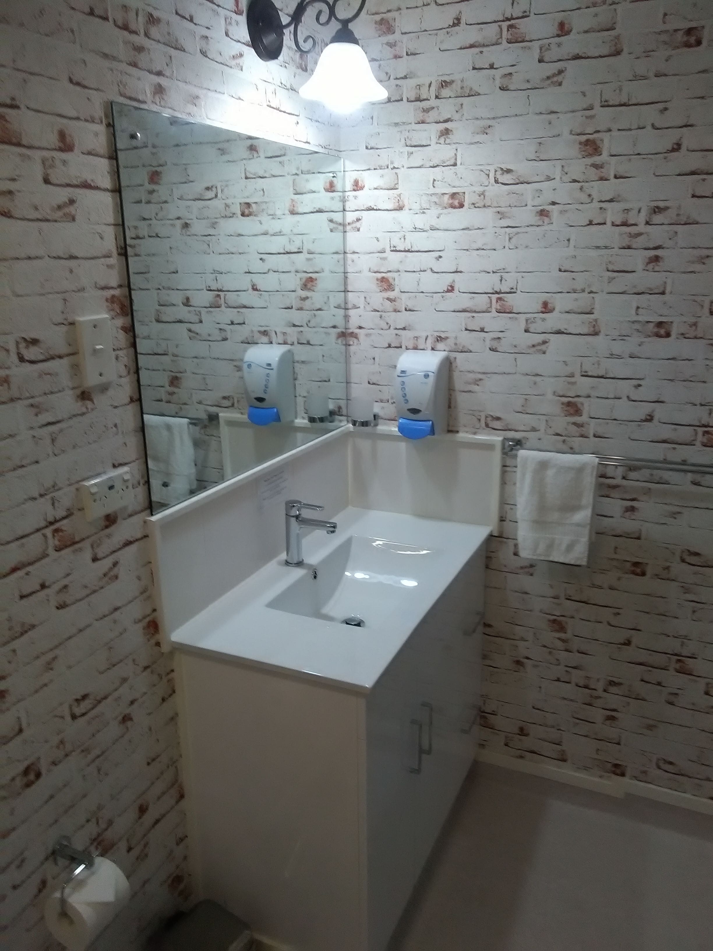 A bathroom with a white sink, a mirror, a towel rack, and a soap dispenser.