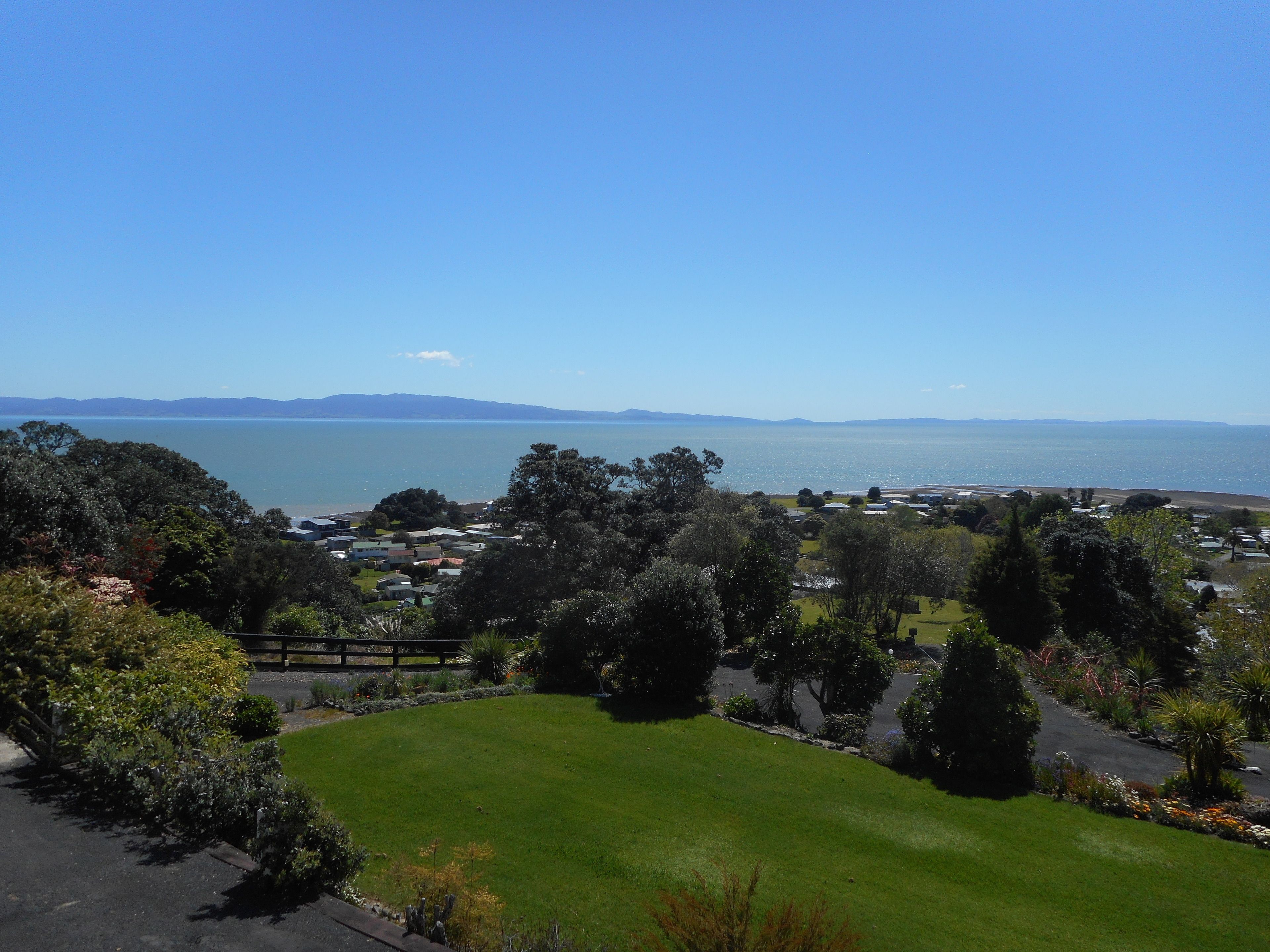 Une vue sur la côte, avec une zone herbeuse, des arbres et une étendue d’eau au loin.