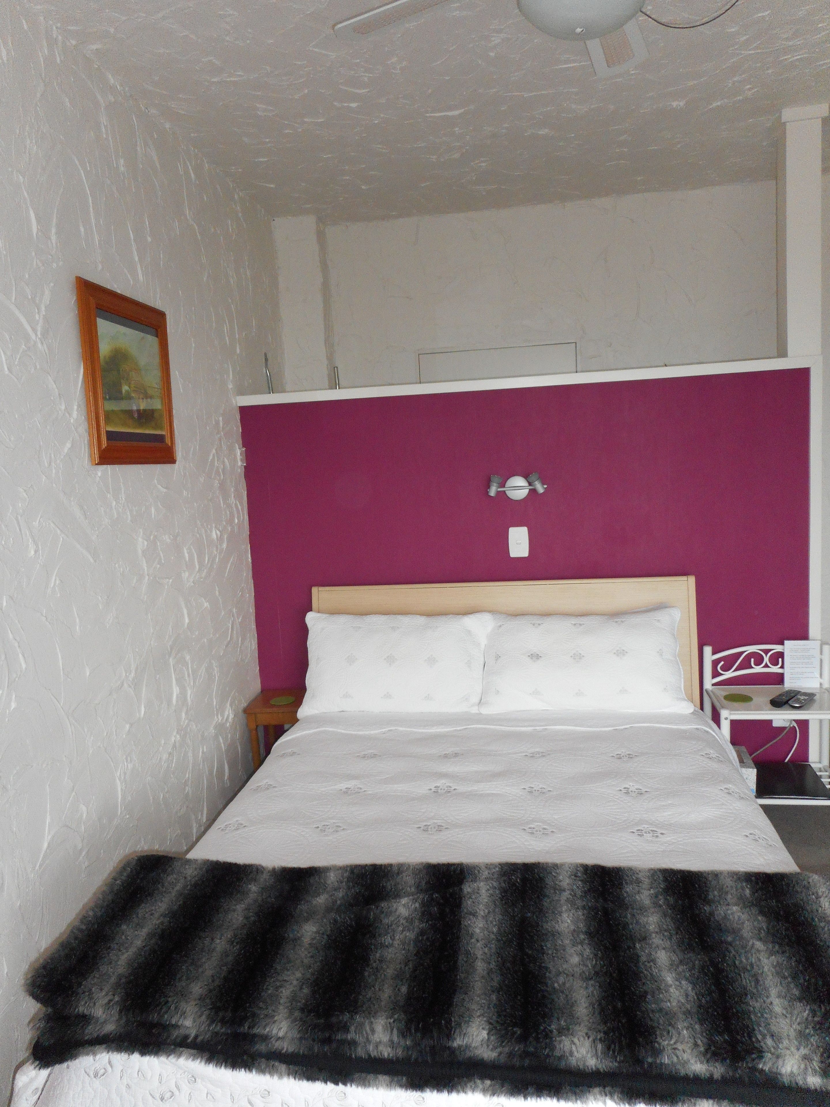 Ein Schlafzimmer mit Bett, Nachttisch, Sessel, einem Bild an der Wand und Deckenventilator.