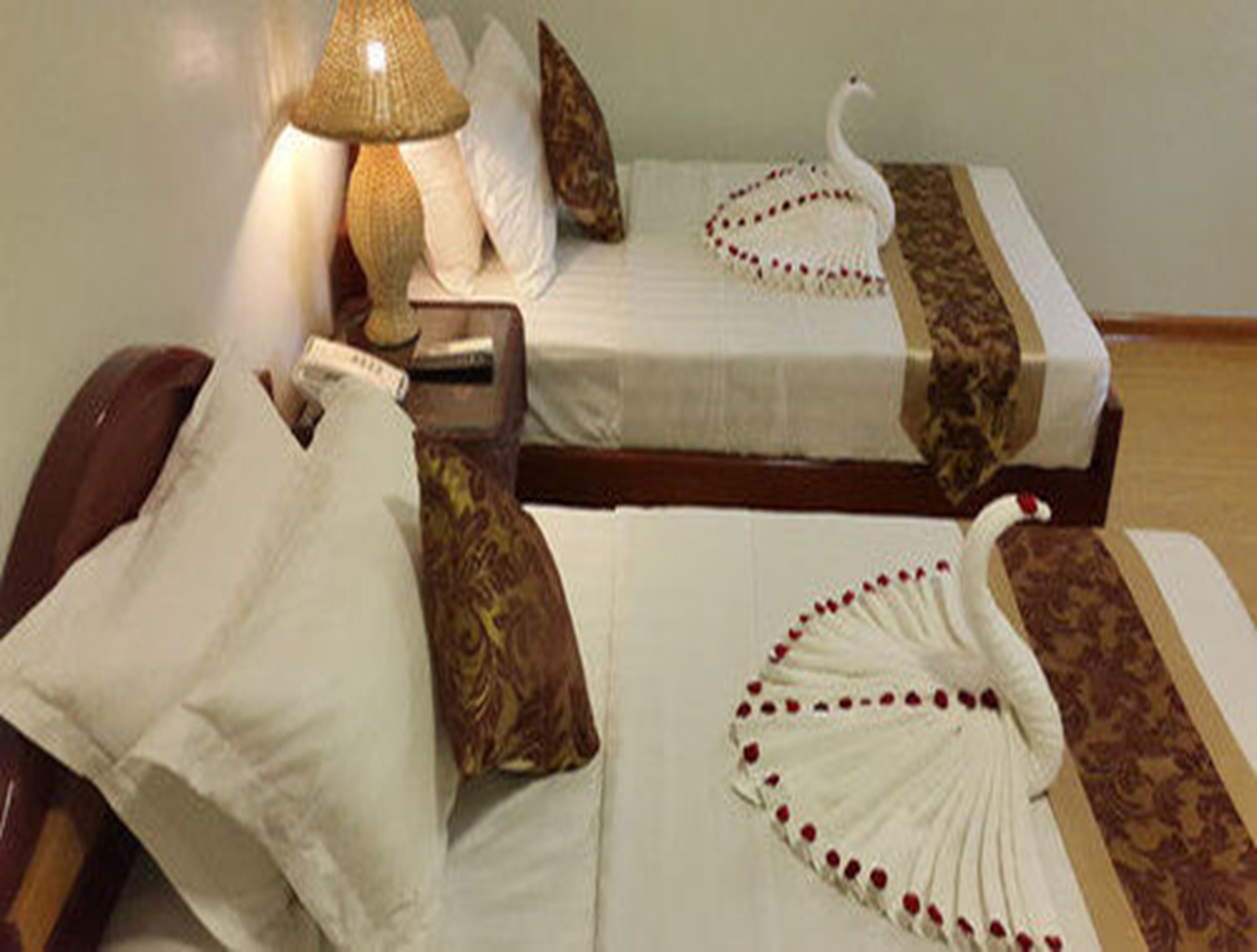 Habitación de hotel con dos camas, cada una con cubrecama blanco y almohadas decorativas. Hay una lámpara en la mesita de noche y un adorno con forma de cisne en una de las camas.
