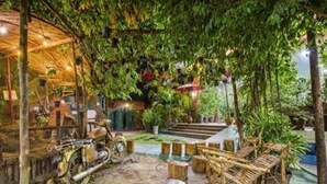 A rustic outdoor area with a motorcycle, wooden seating, and a thatched-roof structure. - Hotel Mega Star (Mandalay)
