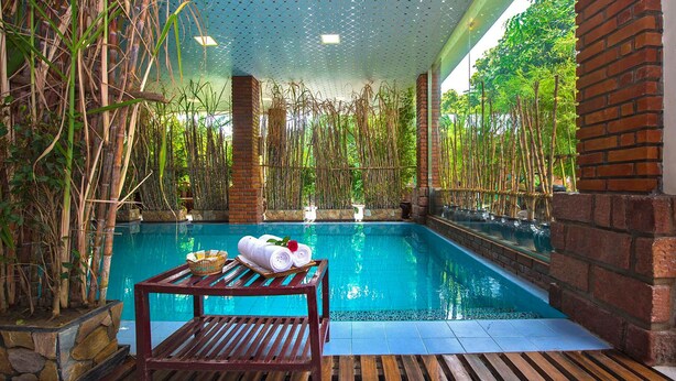 A pool area with bamboo plants, a wooden table with towels, and a brick wall. - Hotel Mega Star (Mandalay)