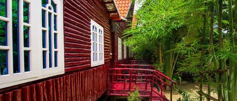 A traditional wooden house with a red exterior, white window frames, and a red staircase leading to a small porch.