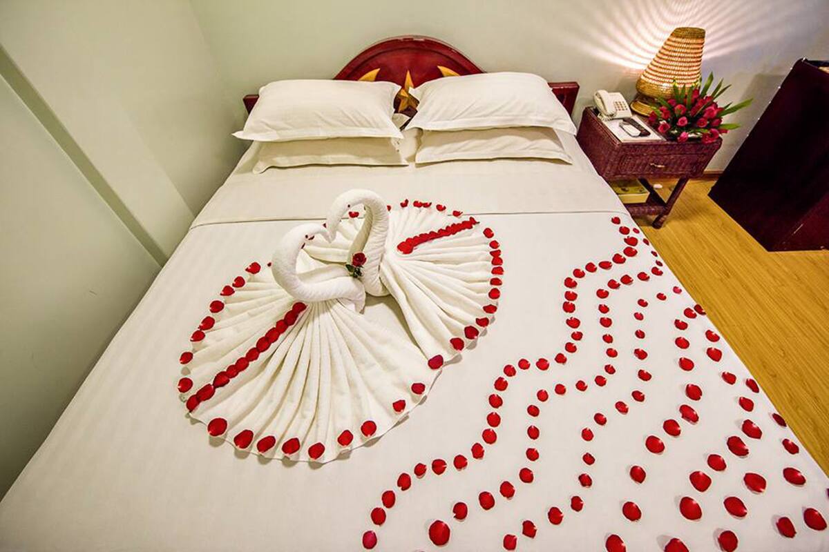 A neatly made bed with a swan towel and rose petals arranged on the bed.