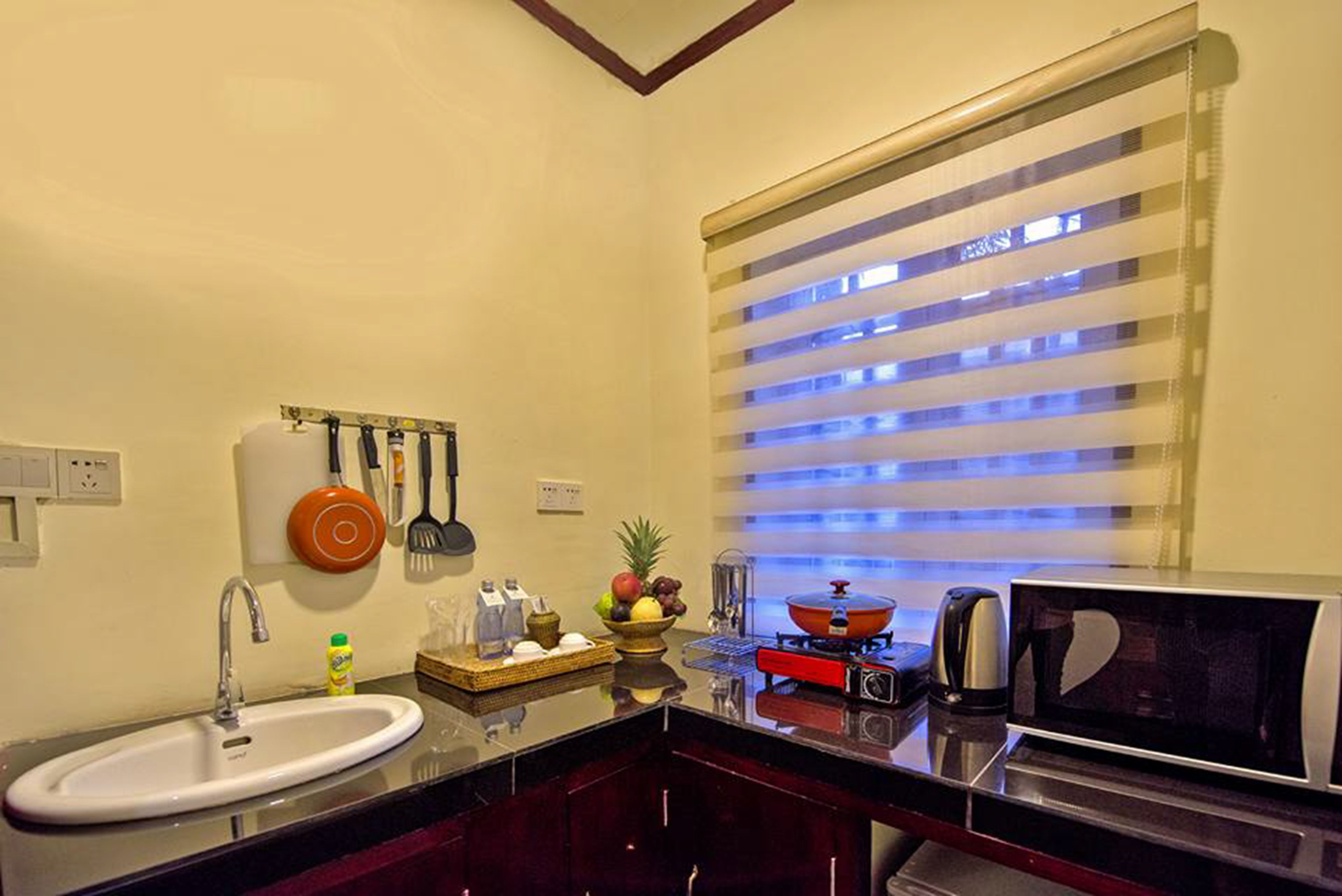 A compact kitchen with a sink, a microwave, and a stove. There are utensils hanging on the wall and a fruit bowl on the counter.