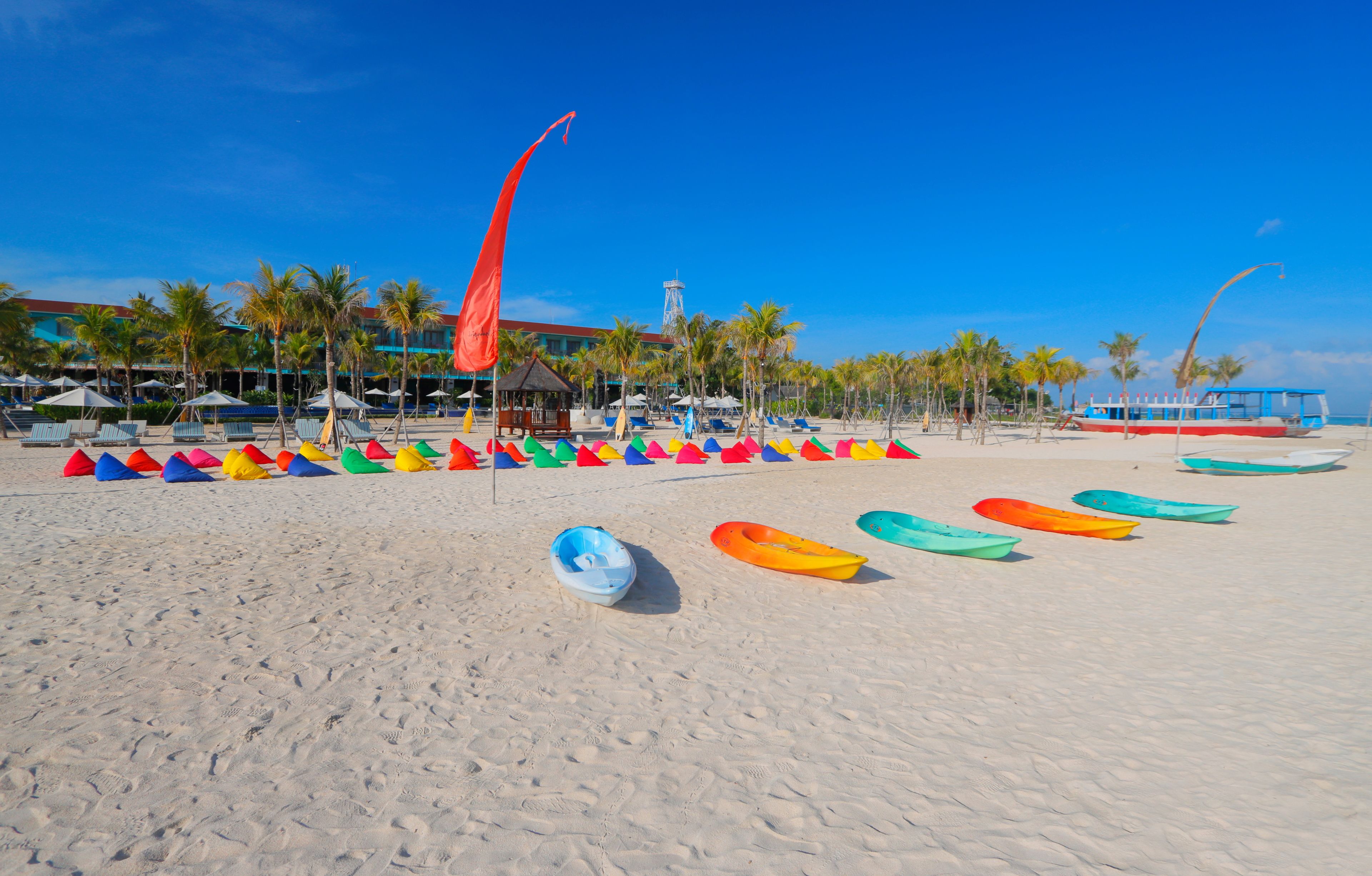 A beach with colorful kayaks lined up and a building with a tower in the background.