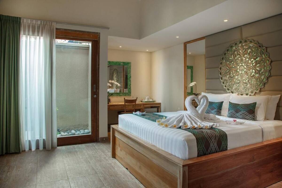 Ein Hotelzimmer mit einem Bett, einem Schreibtisch, einem Stuhl, einem großen Spiegel und Blick durch eine Glastür.