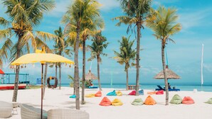 A beach with palm trees, colorful bean bags, and a yellow umbrella. - Mahagiri Resort Nusa Lembongan (Lembongan Island)