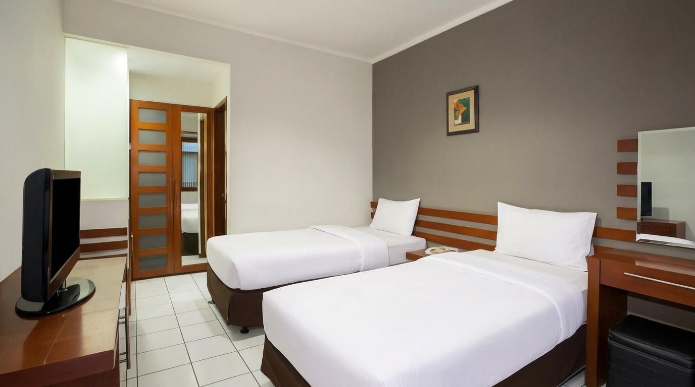 A hotel room with two beds, a television, a desk with a computer, and a bathroom with a shower.