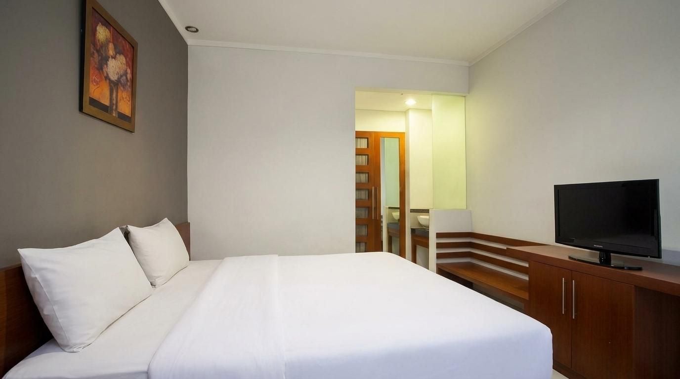 A hotel room with a bed, a television, and a wooden cabinet.